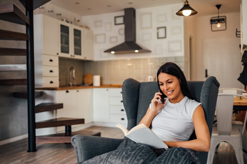 Beautiful woman sitting in armchair at home. Reading a book and having a phone call, portrait.